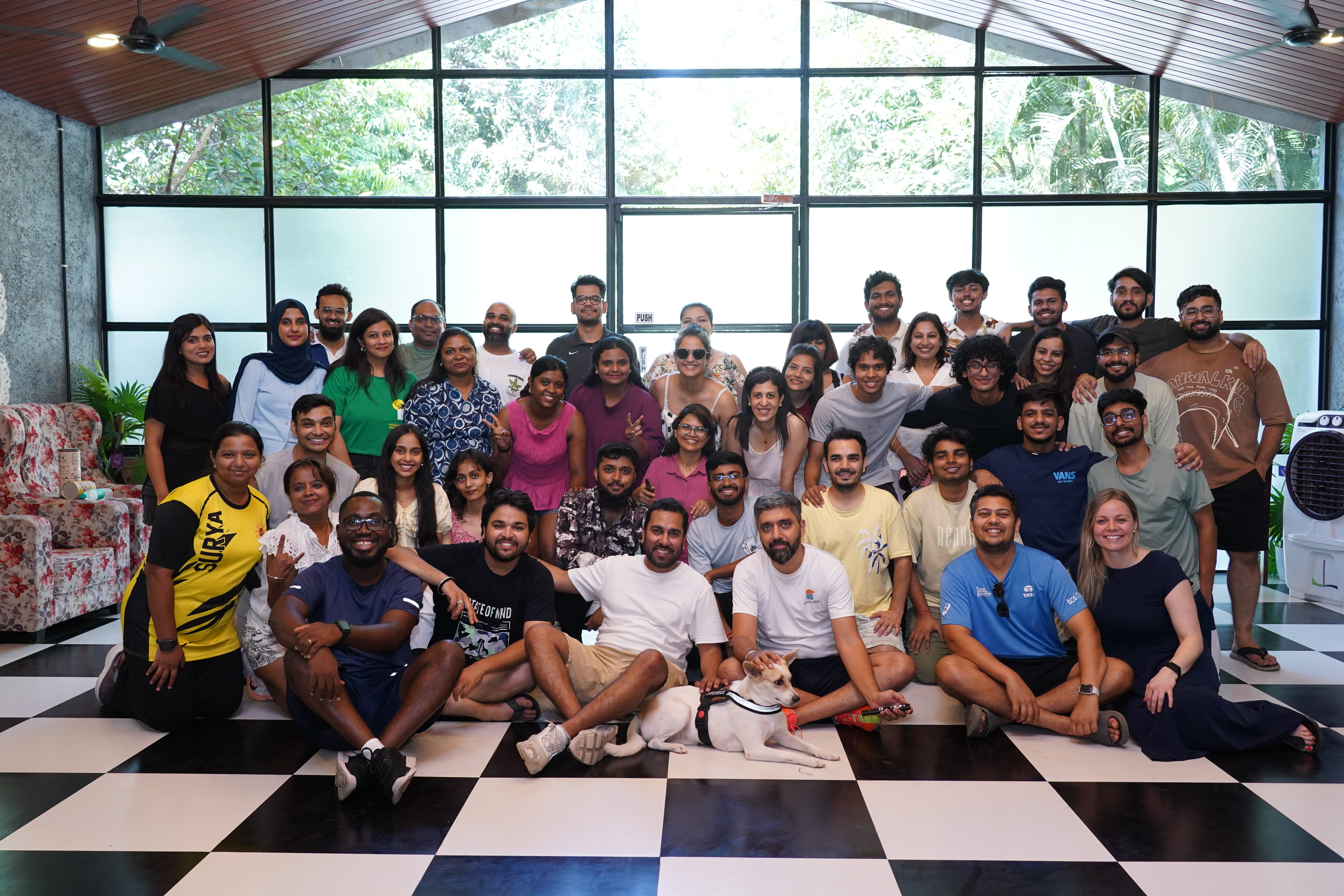 About forty colleagues together in a glass-walled room, seated and standing across a chequerboard floor