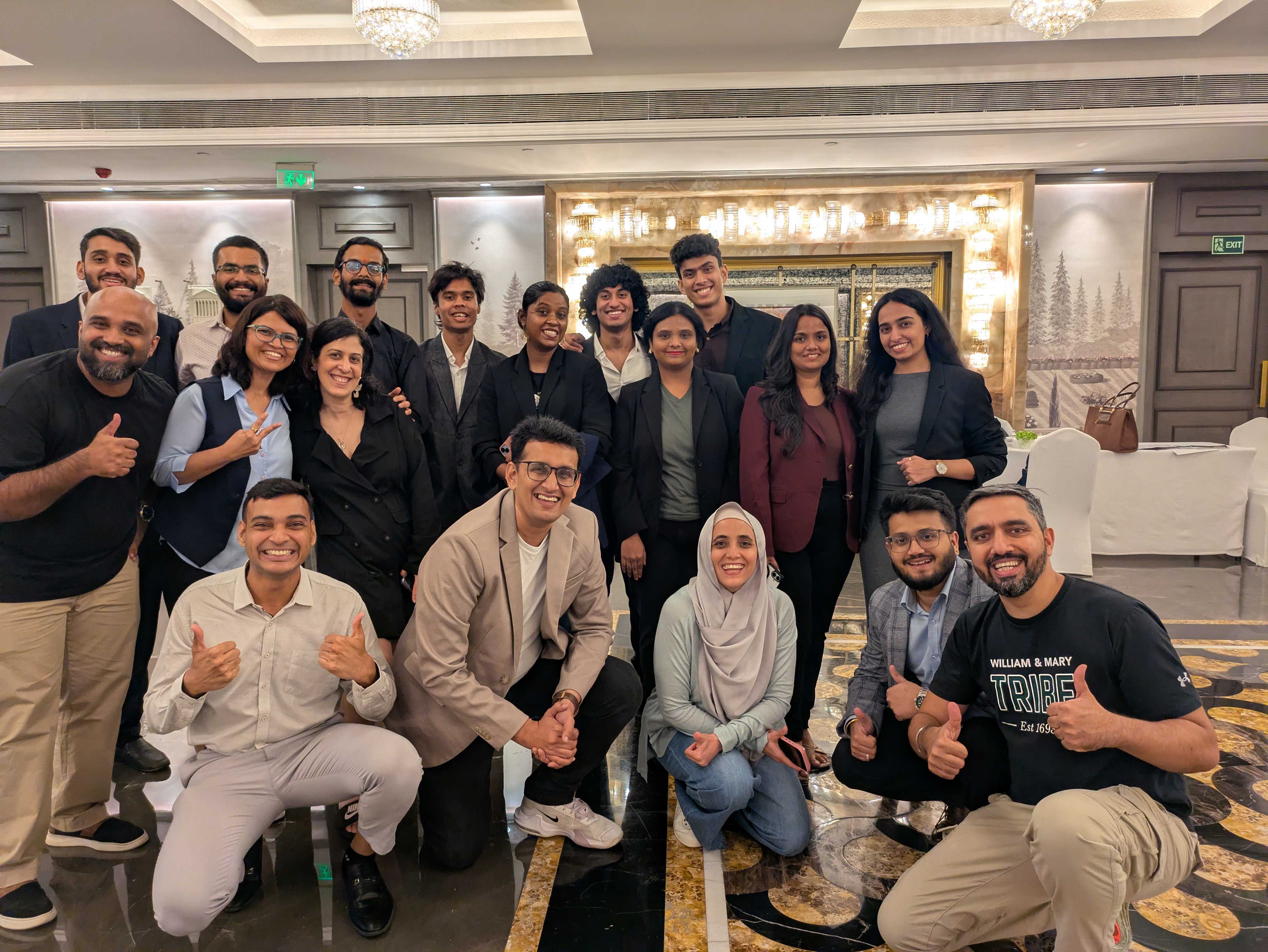 Around twenty of the team in a hotel lobby, several giving a thumbs up